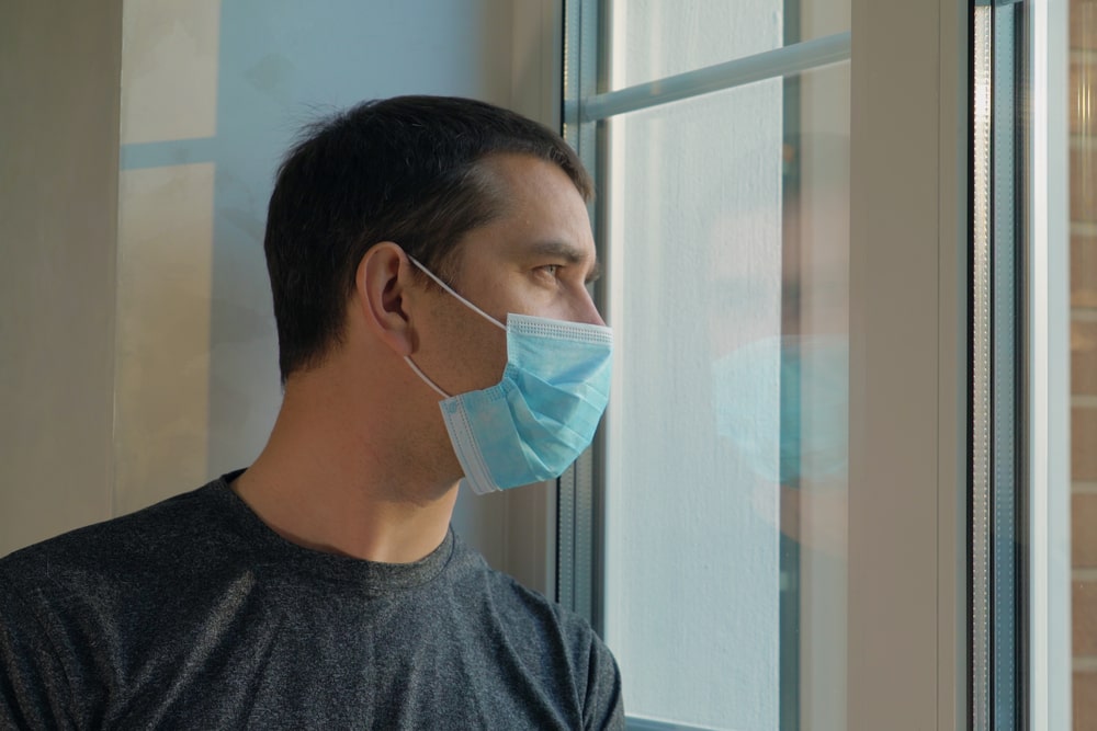 Un uomo guarda dalla finestra indossando la mascherina